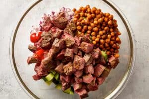 Add the cherry tomatoes, cucumber, red onion, avocado, roasted chickpeas and cubed steak to a large bowl.