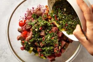 pouring chimichurri over steak chickpea salad in a bowl
