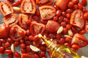 Roma and cherry tomatoes with garlic on a baking tray, drizzled with olive oil and seasoned with salt and pepper before roasting.