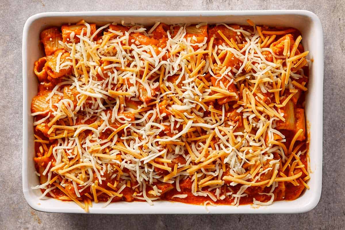 Tomato pasta mixture transferred to a baking dish and topped with shredded cheddar and mozzarella cheese before baking.