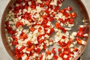 Chopped onion and red bell pepper cooking in a pan until soft and slightly translucent.