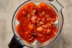 Roasted tomato, onion, garlic, and broth mixture in a blender, ready to be blended into a smooth tomato soup.