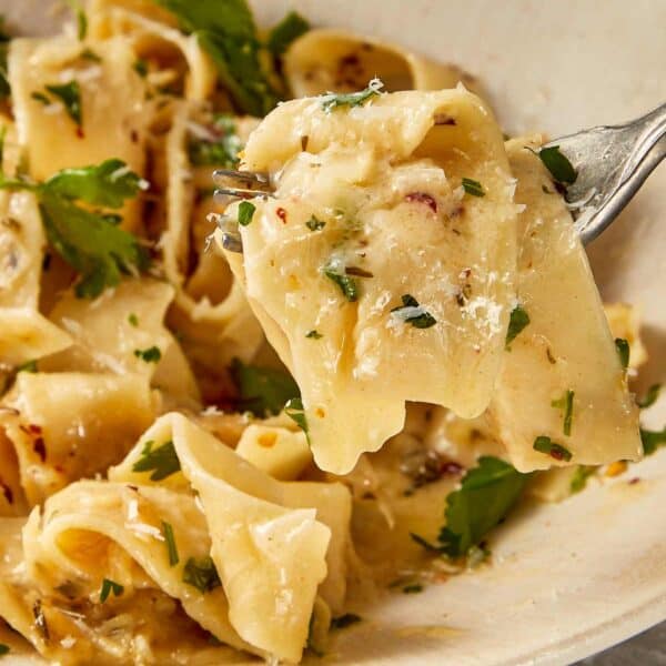 Brown butter Alfredo pasta coated in a creamy parmesan sauce with garlic, shallots, herbs and chilli flakes, finished with fresh parsley and served in a bowl with a fork lifting a bite.
