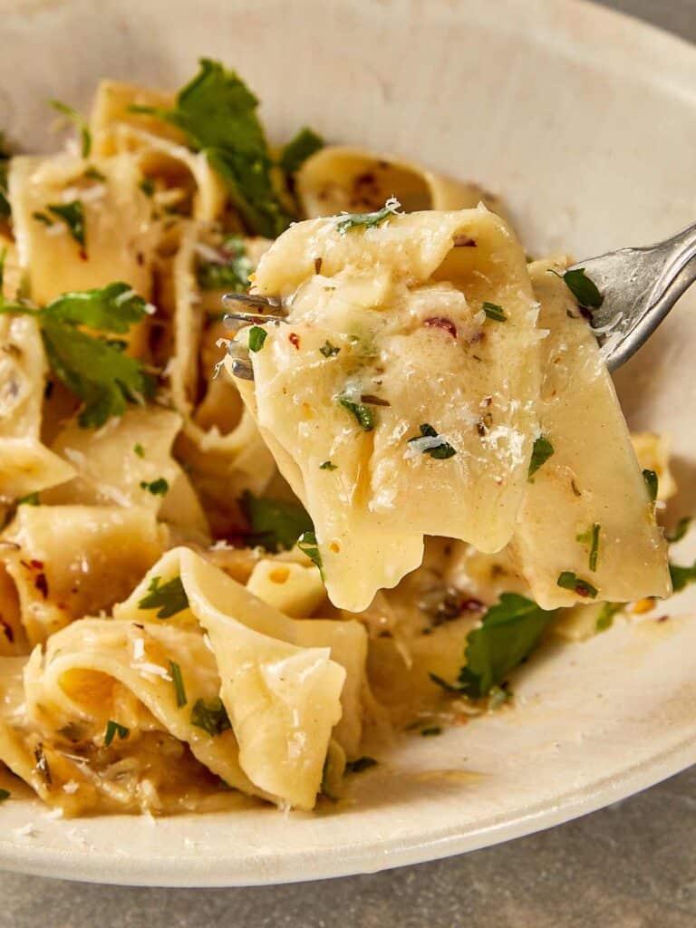 Brown butter Alfredo pasta coated in a creamy parmesan sauce with garlic, shallots, herbs and chilli flakes, finished with fresh parsley and served in a bowl with a fork lifting a bite.