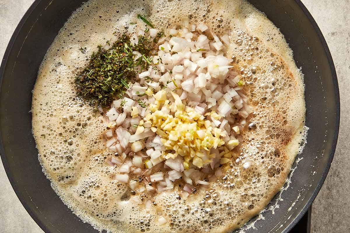 Shallots, garlic, thyme and rosemary added to browned butter, cooking until fragrant.