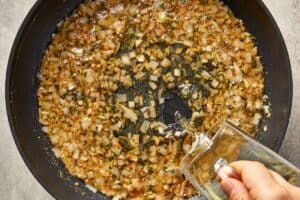 White wine being added to sautéed shallots and garlic in browned butter to deglaze the pan.