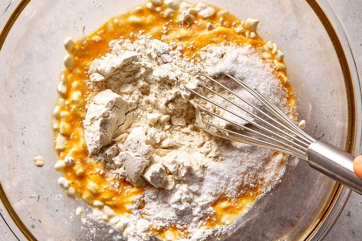 Cottage cheese, egg, and dry ingredients including flour and baking powder combined in a bowl with a whisk, ready to be mixed into pancake batter.
