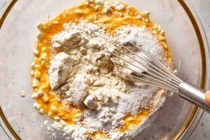 Cottage cheese pancake batter in a mixing bowl with eggs, flour, and baking powder, being combined with a whisk.