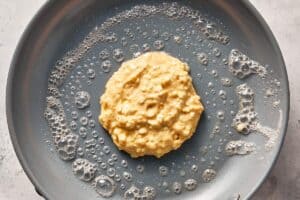 Cottage cheese pancake batter spooned onto a buttered pan, starting to cook into a thick, round pancake.