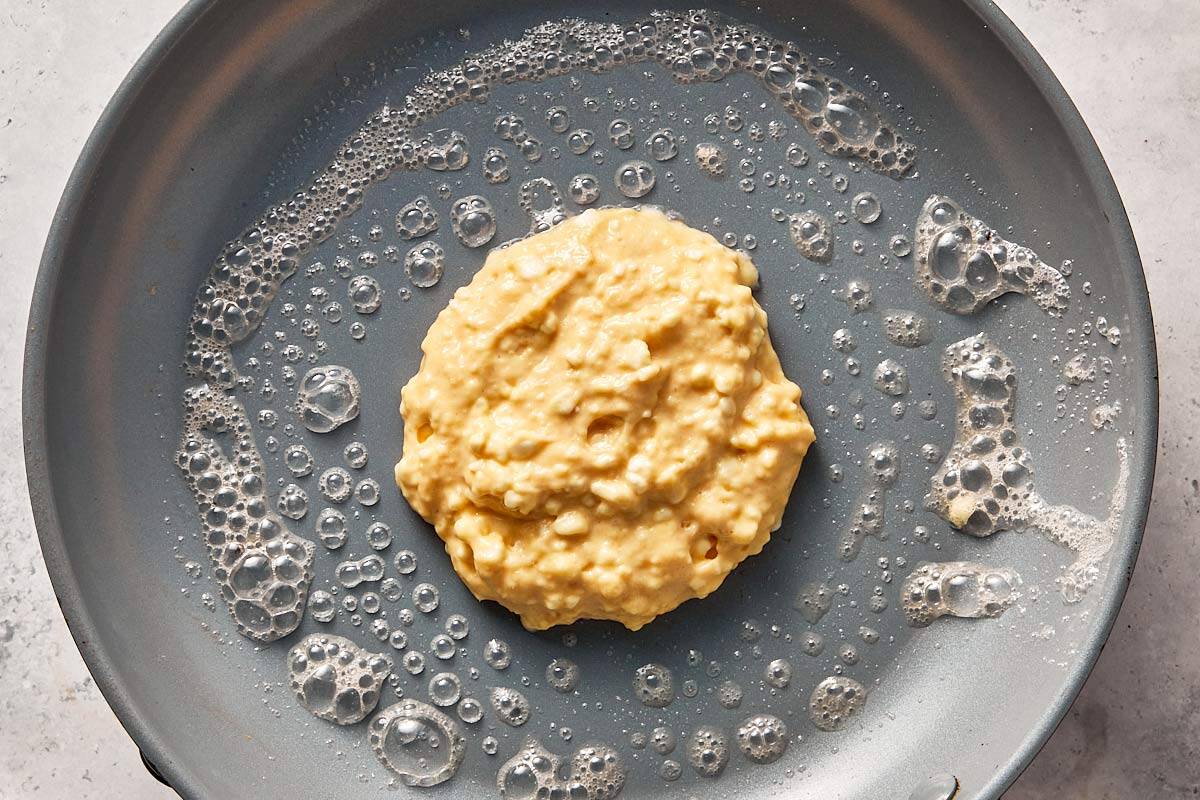 Cottage cheese pancake batter spooned onto a buttered pan, starting to cook into a thick, round pancake.