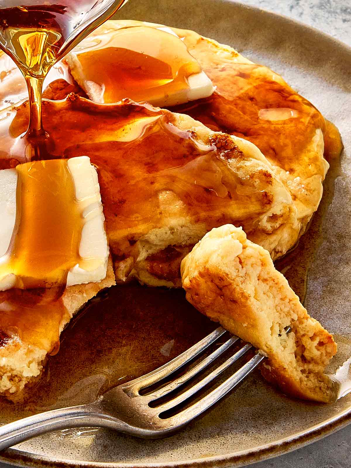 Cottage cheese pancakes stacked on a plate with butter melting on top, drizzled with maple syrup, and a fork cutting into a soft, fluffy bite.