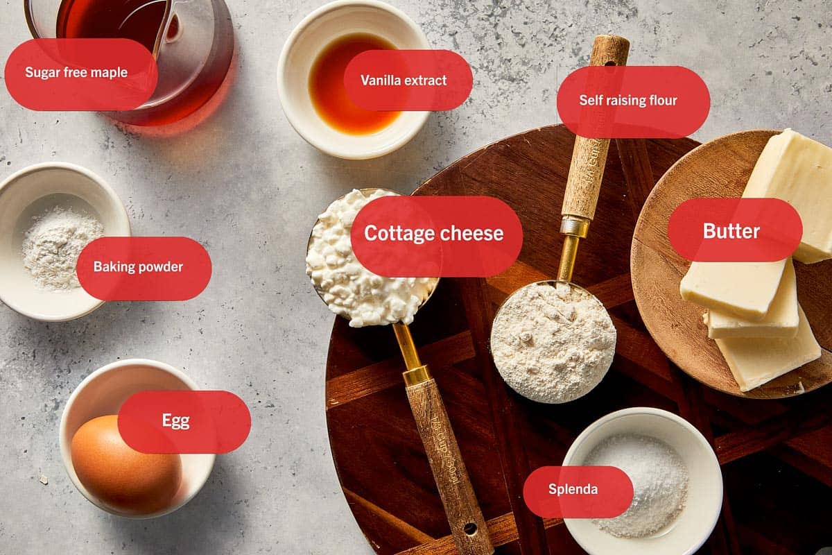Ingredients for cottage cheese pancakes arranged on a surface, including cottage cheese, egg, self-raising flour, butter, baking powder, vanilla extract, Splenda, and sugar-free maple syrup.