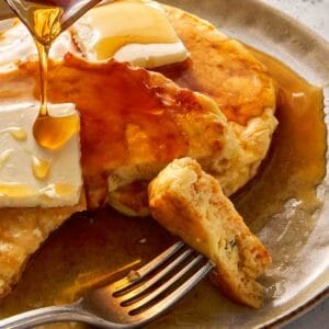 Close-up of cottage cheese pancakes with butter melting on top, maple syrup being poured over, and a fork lifting a soft, fluffy bite.