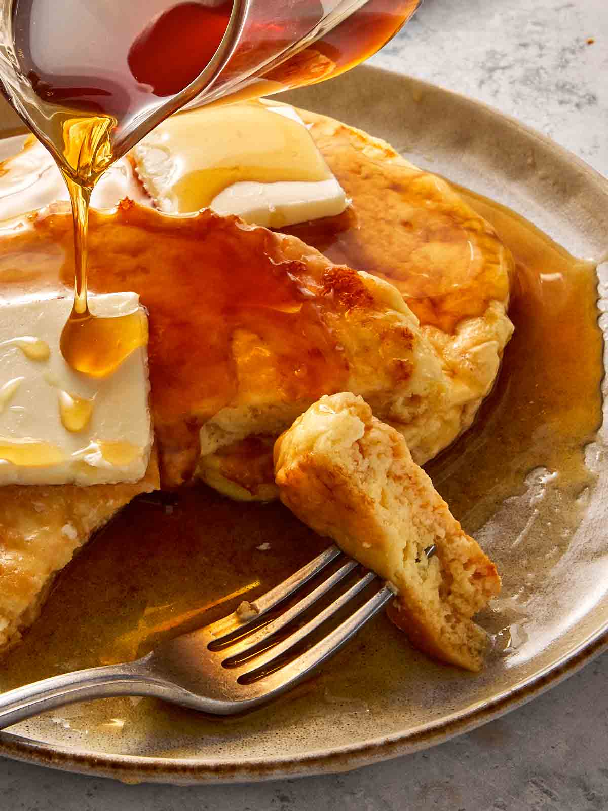 Close-up of cottage cheese pancakes with butter melting on top, maple syrup being poured over, and a fork lifting a soft, fluffy bite.