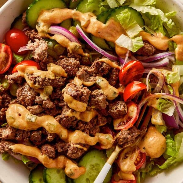Burger bowl with ground beef, cucumber, cherry tomatoes, red onion, lettuce, and creamy burger sauce drizzled on top.