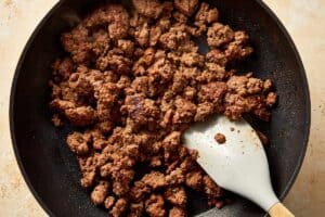 Cooked ground beef browned and crumbled in a skillet with a spatula.