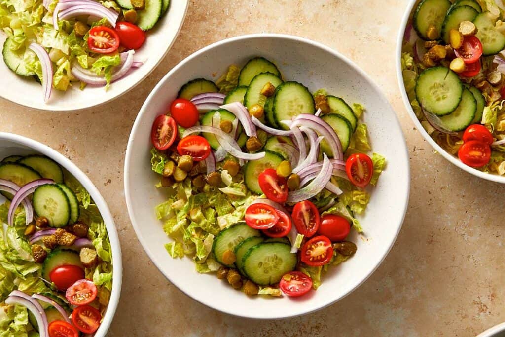 Burger bowls topped with cucumber slices, cherry tomatoes, red onion, and pickles.