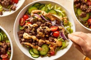 Burger bowl finished with creamy sauce drizzled over beef, vegetables, and lettuce.