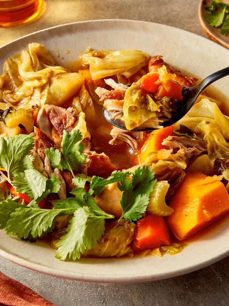 Healthy cabbage chicken soup for weight loss with shredded chicken, pumpkin, carrots, and cabbage in a flavorful broth topped with fresh cilantro