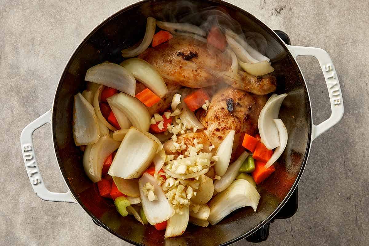Cooking vegetables with chicken for cabbage chicken soup including onion, carrot, celery, and garlic in a pot