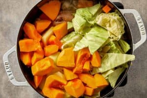 Pumpkin, potato, and cabbage added to cabbage chicken soup with chicken in a pot before simmering