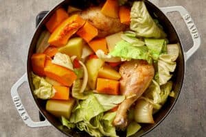 Cabbage, pumpkin, and potato mixed with chicken and seasoning in a pot for cabbage chicken soup