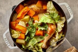 Chicken cabbage soup in a large pot with pumpkin, potatoes, carrots, and fresh cabbage, topped with cilantro before adding the broth