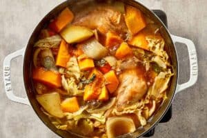 Cabbage chicken soup simmering in broth with chicken, cabbage, pumpkin, and vegetables cooking together