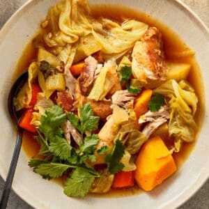 Shredded chicken cabbage soup with pumpkin, potatoes, carrots, and celery in a light, flavorful broth, topped with fresh cilantro in a bowl