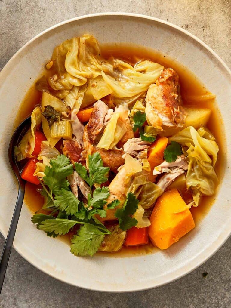 Shredded chicken cabbage soup with pumpkin, potatoes, carrots, and celery in a light, flavorful broth, topped with fresh cilantro in a bowl