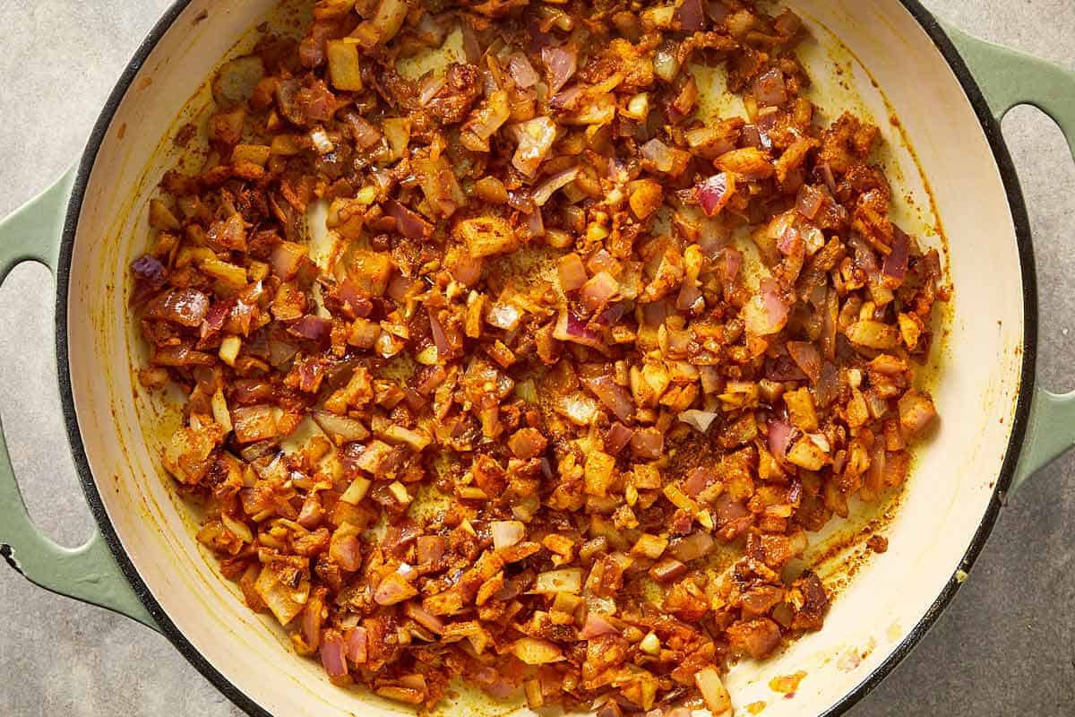 Cooked onions mixed with garlic, ginger, and spices in a pan.