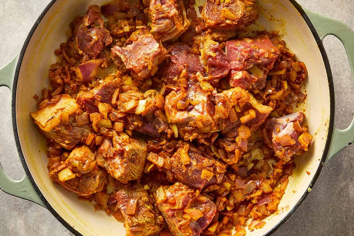 Lamb pieces coated in spices and onions while cooking.
