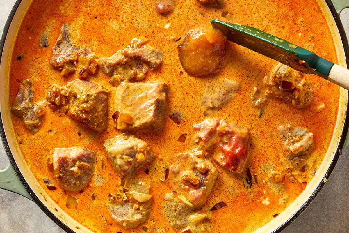 Lamb curry mixture being stirred into a creamy sauce.