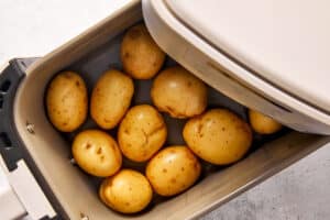 Baby yellow potatoes cooking in an air fryer basket, arranged in a single layer before roasting