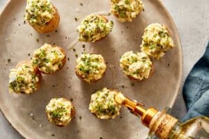 Deviled potatoes filled with creamy egg mixture and topped with chives, black pepper, and olive oil on a serving plate