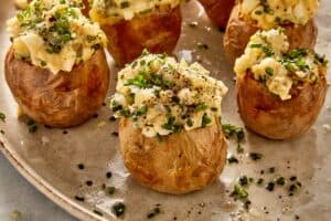 Deviled potatoes filled with creamy egg and potato mixture, topped with chives, pickles, and black pepper, served on a plate