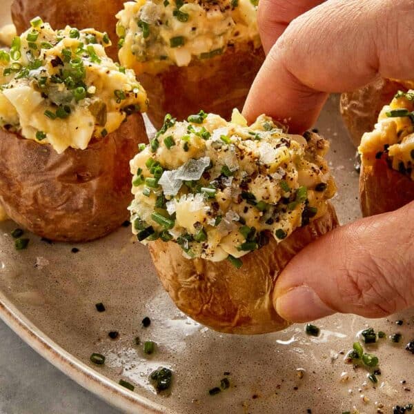 Hand picking up a deviled potato filled with creamy egg and potato filling and topped with chives