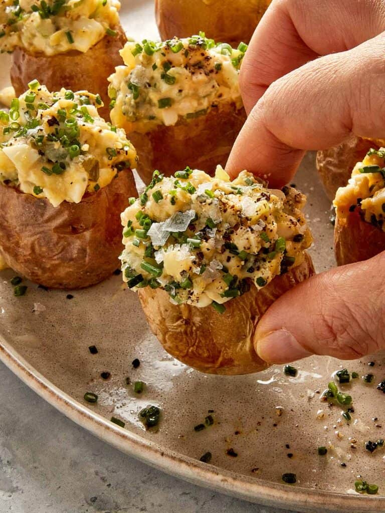 Hand picking up a deviled potato filled with creamy egg and potato filling and topped with chives