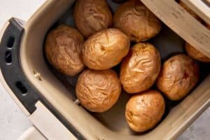 Cooked baby potatoes in an air fryer basket, with wrinkled skins and tender centers ready to be filled