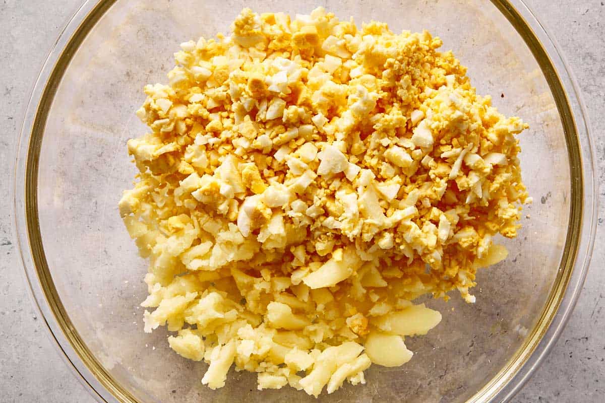Mashed potato filling combined with chopped hard-boiled eggs in a mixing bowl for deviled potatoes