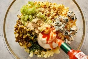 Potato and egg mixture combined with mayo, mustard, pickles, celery, chives, blue cheese, and hot sauce in a bowl for deviled potato filling