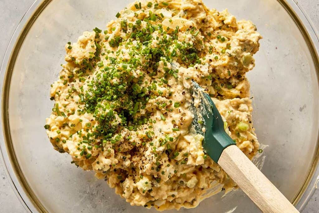 Creamy deviled potato filling mixed in a bowl with chopped chives and black pepper, ready to be spooned into potatoes