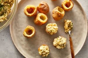 Deviled potatoes being filled with creamy egg and potato mixture using a spoon, with hollowed baby potatoes on a plate