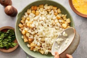 Adding chopped onion to cooked potatoes in pan