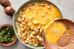 Pouring beaten eggs over potatoes and onions in pan