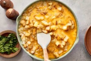 Mixing eggs with potatoes and onions in pan