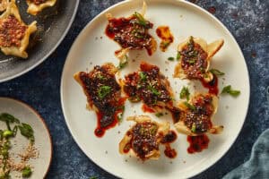 Finished pan dumplings on a white plate, topped with chili sauce, green onions, and sesame seeds.