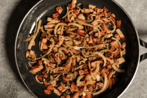 Chopped bacon and onion in a pan being cooked in a medium heat