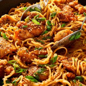 Close-up of honey sesame chicken noodles with a spoon