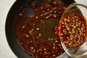 Pan being poured the sauce for the sesame chicken noodles